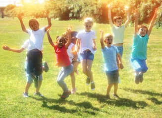 Naklejka na ściany i meble Group of happy children jumping and smiling together in park