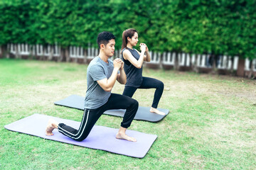 Young Asian couple playing yoga together in thier home garden on holiday, family concept.