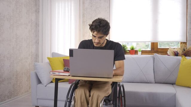 Disabled young man working hard with laptop.
Disabled teenager working at home focused on laptop.
