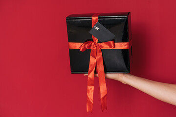 On the hand lies glossy gift box with red bow and credit card.