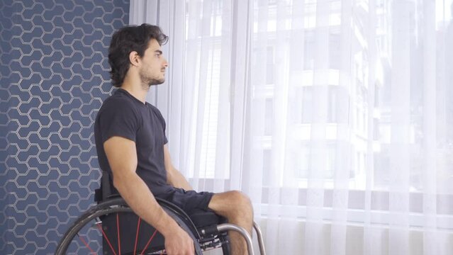Young disabled person sitting in a wheelchair watching out the window at home.
Unhappy disabled man looking out the window, feeling sad and helpless at home.
