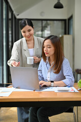 Asian female office worker working with her professional boss in the office, using laptop