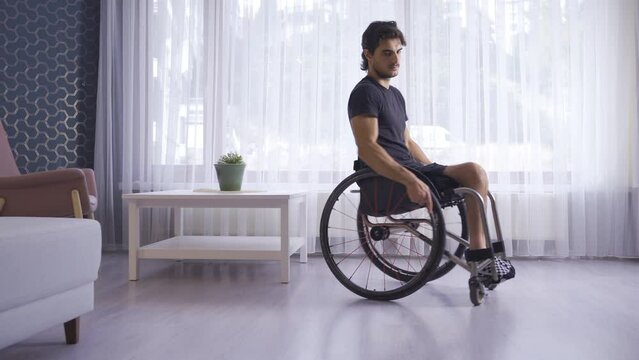 Disabled youth in a wheelchair at home.
Disabled young man is thoughtful and looks out the window of the house.
