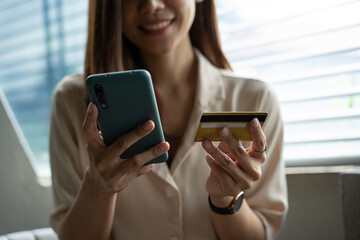 Young Asian woman using credit card and mobile phone for online shopping in coffee shop or coworking space