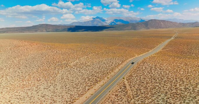 Lonely black car on the road to Nevada, USA. Beautiful sight of desert contrasting with blue skies. Mountains at backdrop.