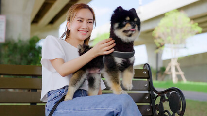 Happy young asian woman playing and sitting on a bench in the park with her dog. Pet lover concept