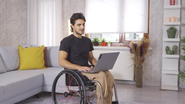 Disabled young man working with laptop in slow motion.
Disabled young man working at home looking at laptop.
