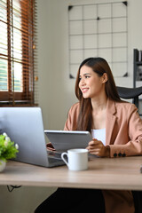 Successful Asian businesswoman at her office desk, looking through the window, daydreaming