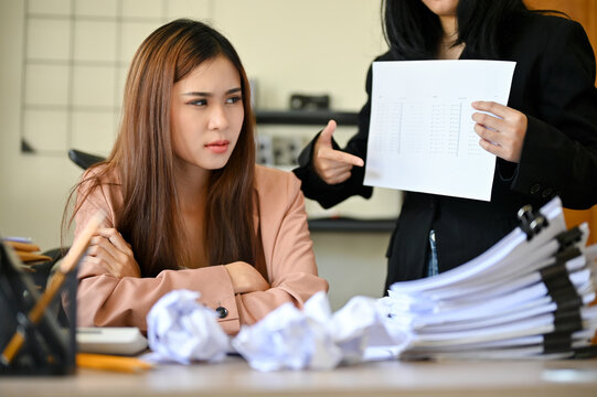 Unhappy And Overworked Asian Female Employee Receiving Work Complaints From Her Boss. 