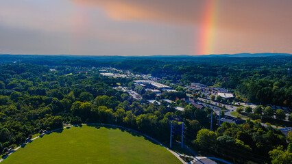 an aerial shot of the vast miles of lush green trees and grass with buildings nestled among the trees and powerful clouds and a rainbow at Etowah River Park in Canton Georgia USA - obrazy, fototapety, plakaty