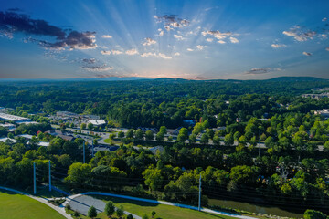an aerial shot of the vast miles of lush green trees and grass with buildings nestled among the trees and powerful clouds at sunset at Etowah River Park in Canton Georgia USA - obrazy, fototapety, plakaty