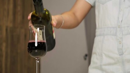 A modern personality woman pours her red wine into a wine glass at a romantic restaurant. New Year and Christmas celebration ideas
