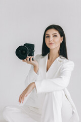 Portrait of a smiling young woman in a white suit holding a camera. Isolated white background and education concept. 