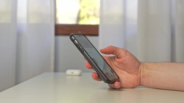 A young man uses his iPhone with a protective black bumper to thumb type a quick note to himself