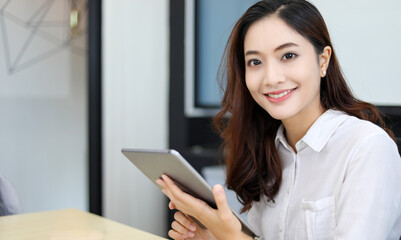 Fototapeta premium Smiling Asian businesswoman using tablet for work and doing internet research in her office.