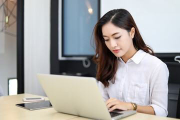 Asian businesswoman using laptop for work and doing internet research in her office.
