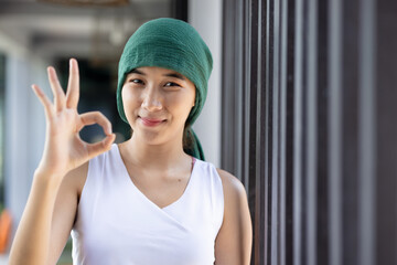 Happy smiling asian woman cancer patient wearing head scarf for hair loss, showing ok hand gesture...