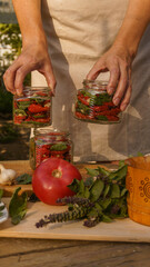 a woman preserves sun-dried tomatoes in sterile jars with chopped garlic and fresh basil in the garden at sunset. hands close-up, rich harvest, organic natural products, preparations for the winter