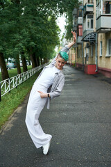 A woman with green hair in white clothes and with an umbrella walks down the street after the rain