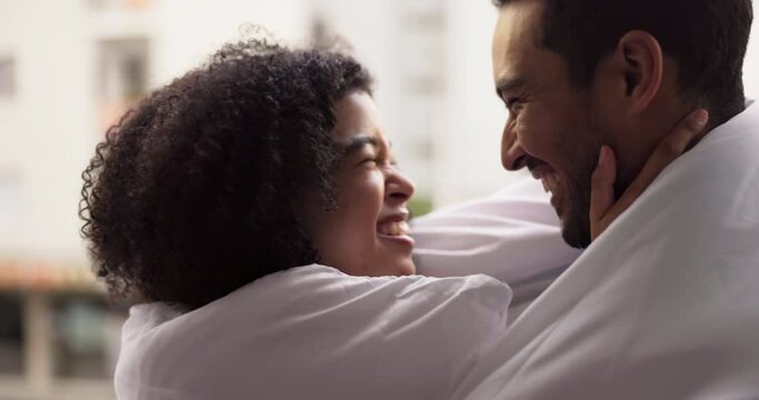 Happy couple kiss, dancing in the hotel apartment room playfully and smile with love in a blanket. Black woman with her partner on holiday, relax and bond in their holiday home enjoying time together