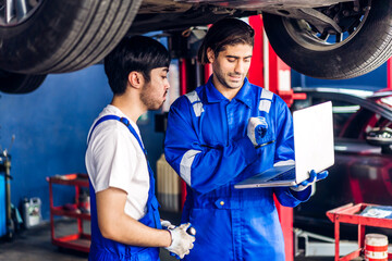 Professional car technician mechanic team in uniform use laptop work fixing vehicle car engine and...