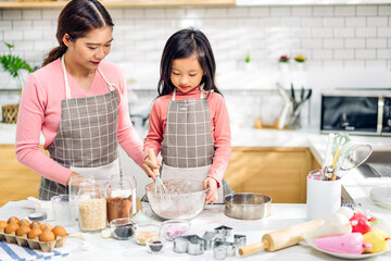 Portrait of enjoy happy love asian family mother and little toddler asian girl daughter child having fun cooking together with dough for homemade bake cookie and cake ingredient on table in kitchen