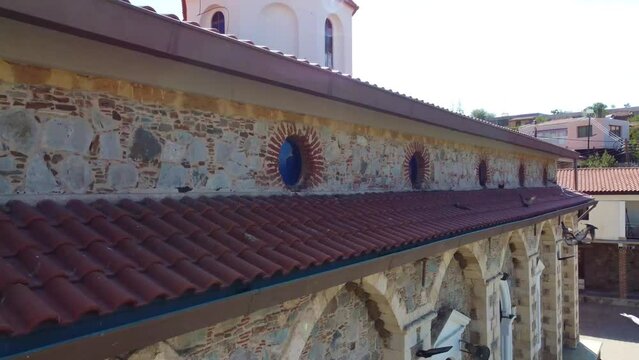 Aerial drone footage of traditional village Farmakas, Nicosia, Cyprus. Establish scene of christian church Saint Irene with ceramic tiled roof dome and volcanic rock architecture from above.