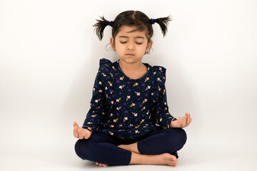 Charming little girl doing serious yoga meditation in studio with an isolated white background. Little Indian girl kid doing meditation in studio.