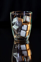 stainless steel cubes simulating ice in whisky glass on a black table.