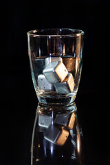 stainless steel cubes simulating ice in whisky glass on a black table.