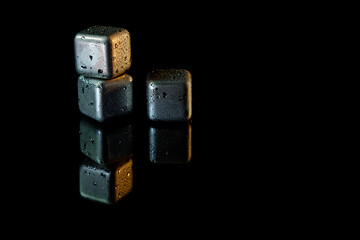 Stainless steel cubes simulating ice for cooling drinks on a black surface with a reflection.