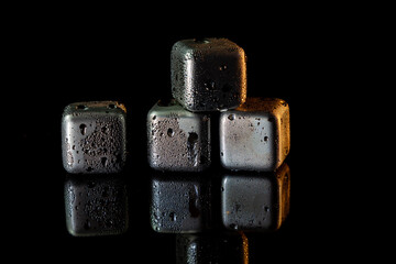 Stainless steel cubes simulating ice for cooling drinks on a black surface with a reflection.