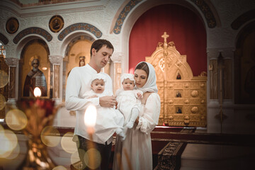 family mom, dad with small twin children in a temple or church praying near an icon and candles or...