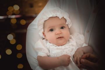 a baby in a baptismal outfit in the arms of his mother in a temple or church came to worship in an...
