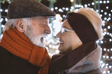 Happy elderly couple smiling in the winter wonderland and twinkle lights