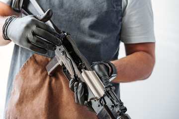 Close up of young man in apron disassembling a gun above the table