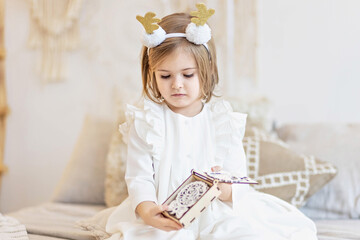 Fototapeta na wymiar Portrait of a little girl Toddler with a headband on her head in the form of deer horns and a Christmas toy in her hands. Christmas holidays.Light and bright