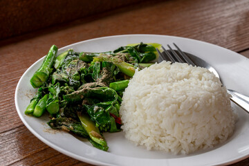 Stir Fried Kale with rice on white plate on wooden table