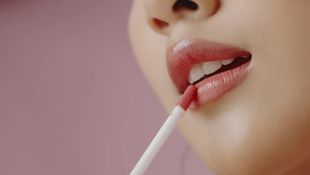 Close up Young Asian woman apply lipstick on her lips isolated on pink background, Slow motion shot.