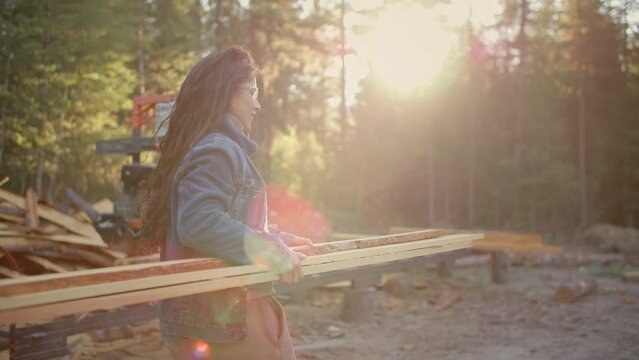 Woodworking female carries pile of wood, golden light