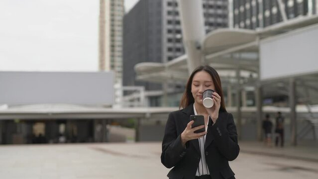 4K video of a professional smart cool asian young attractive businesswoman holding a cup of coffee look around the city with happy satisfied look after finish chatting happily on the phone in a centra