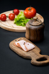 Still life with slices of ham and vegetables over wooden board on a black background
