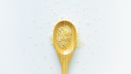 Flavored yellow bath salt in wooden spoon on white background top view