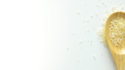 Flavored yellow bath salt in wooden spoon on white background top view
