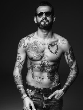 Portrait of handsome confident stylish hipster lambersexual model. Sexy modern man. Naked torso with tattoos.Fashion male posing in studio on dark background. Black and white