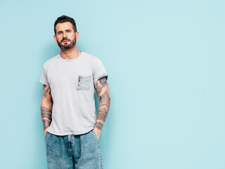 Fototapeta premium Portrait of handsome confident stylish hipster lambersexual model. Sexy man dressed in T-shirt and jeans. Fashion male isolated on blue wall in studio