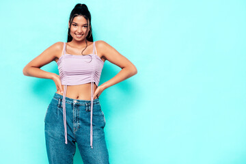Young beautiful smiling female in trendy summer jeans and top clothes. Carefree woman posing near blue wall in studio. Sexy positive model having fun indoors. Cheerful and happy