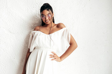 Young beautiful smiling female in trendy summer dress clothes. Sexy carefree woman posing near white wall in studio. Positive model having fun and going crazy. Cheerful and happy. In sunglasses