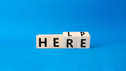 Help is here symbol. Turned wooden cubes with words Here to Help. Beautiful blue background. Business and Help is here concept. Copy space