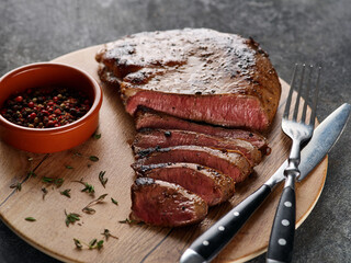 Grilled beef heart steak with pepper on a wooden board.